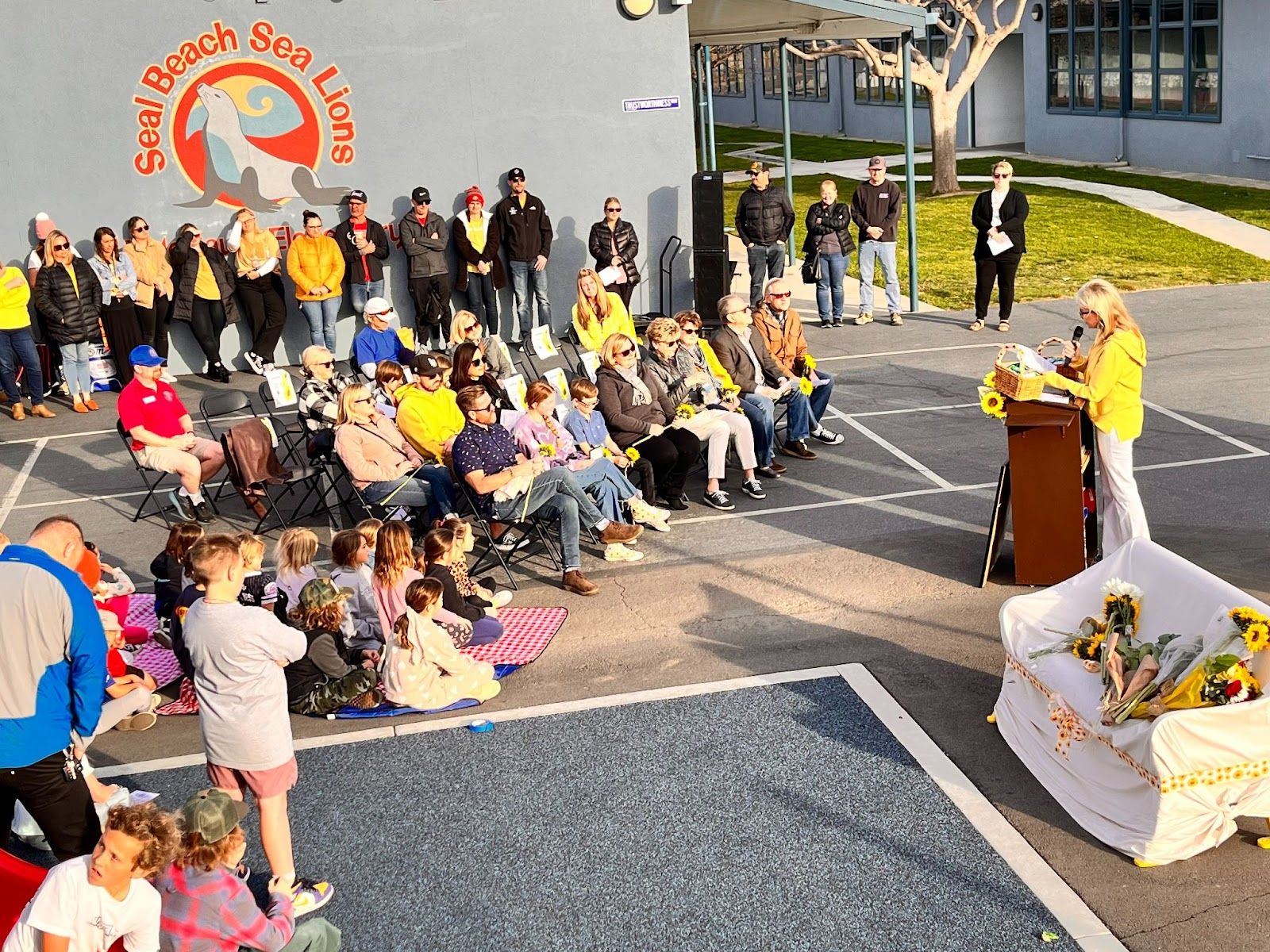 Former McGaugh Elementary School principal Roni Ellis speaks to a crowd at the campus during the bench dedication ceremony for teacher Cari Crevda McQuiston. Photo by Jeannette Andruss.